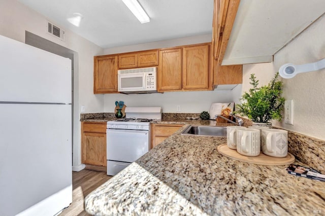 kitchen featuring visible vents, a sink, white appliances, light wood finished floors, and light stone countertops