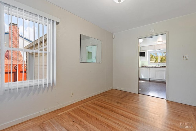 spare room featuring light wood finished floors, a sink, and baseboards