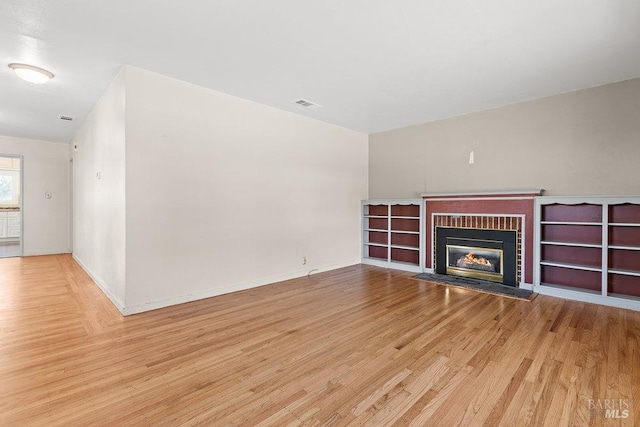 unfurnished living room featuring a fireplace, wood finished floors, visible vents, and baseboards