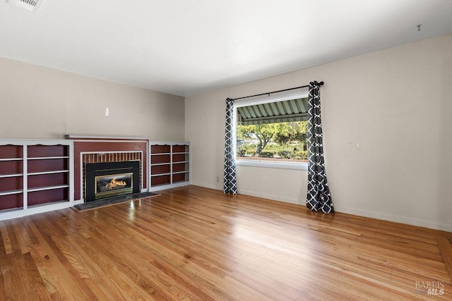 unfurnished living room featuring visible vents, a brick fireplace, wood finished floors, and baseboards