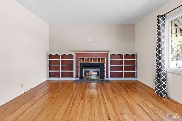 unfurnished living room with baseboards, light wood finished floors, and a fireplace with flush hearth
