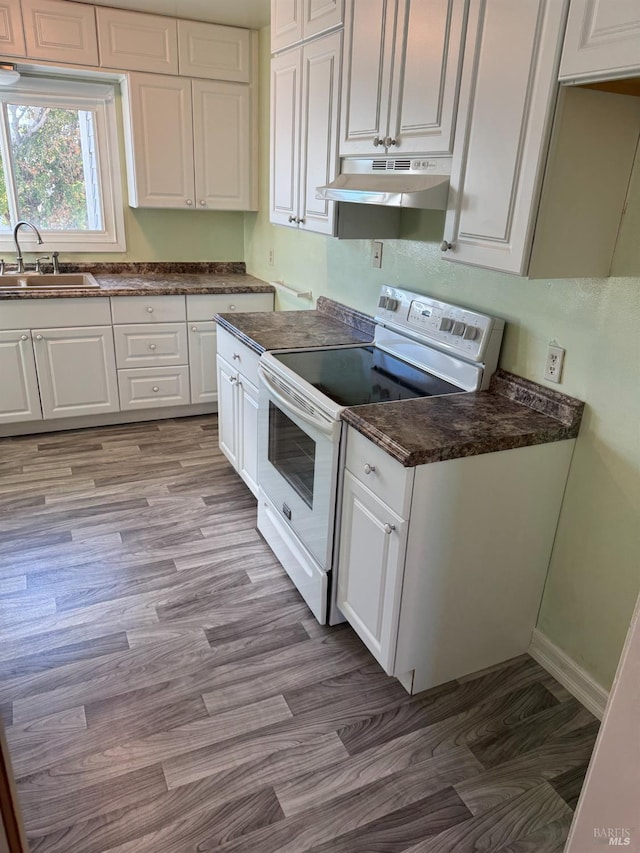 kitchen with under cabinet range hood, a sink, white cabinetry, white range with electric cooktop, and dark countertops