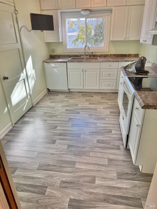 kitchen featuring baseboards, white appliances, light wood-style flooring, dark countertops, and a sink