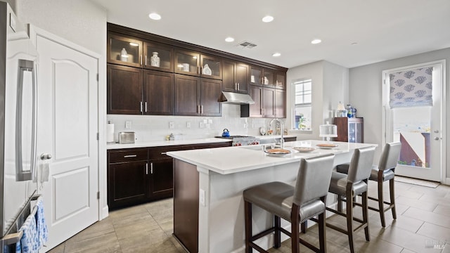 kitchen featuring sink, dark brown cabinets, a kitchen island with sink, a kitchen bar, and decorative backsplash