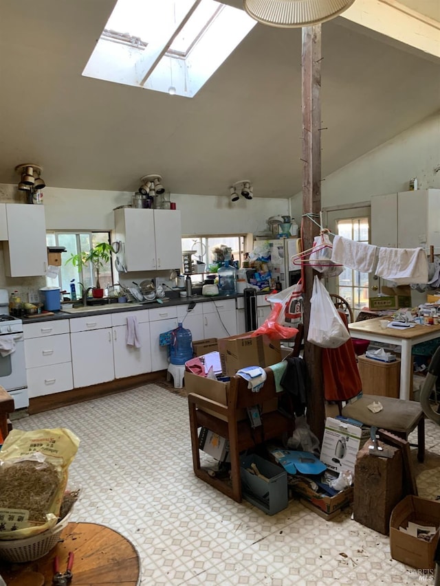 kitchen featuring white cabinets, plenty of natural light, white gas range, and vaulted ceiling with skylight