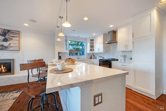 kitchen featuring black gas stove, wall chimney range hood, wood-type flooring, and white cabinets