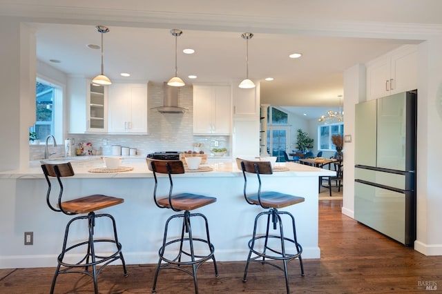 kitchen featuring stainless steel refrigerator, wall chimney exhaust hood, a kitchen bar, and white cabinetry