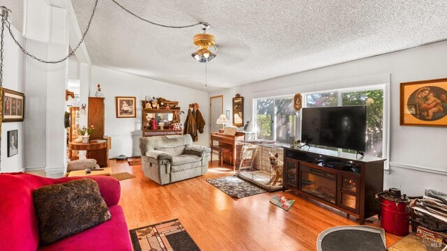 living room featuring ceiling fan, hardwood / wood-style flooring, lofted ceiling, and a textured ceiling