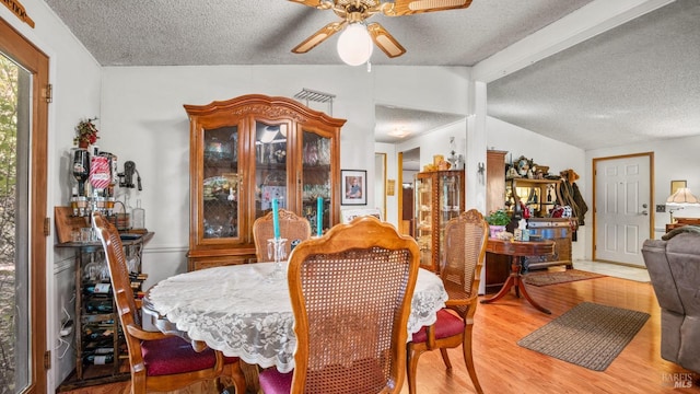 dining space with ceiling fan, vaulted ceiling with beams, hardwood / wood-style floors, and a textured ceiling