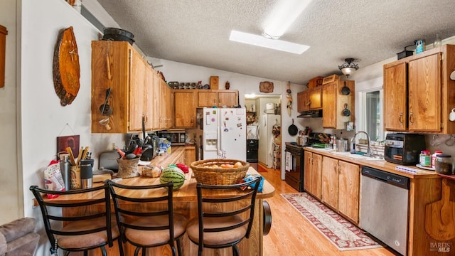 kitchen featuring light hardwood / wood-style floors, vaulted ceiling, sink, stainless steel appliances, and a textured ceiling