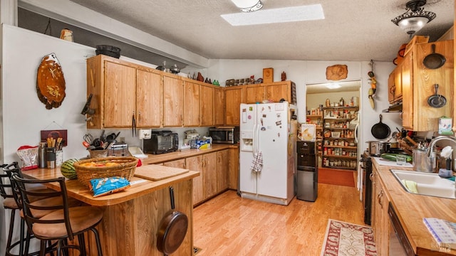 kitchen with vaulted ceiling with skylight, light wood-type flooring, sink, appliances with stainless steel finishes, and a textured ceiling