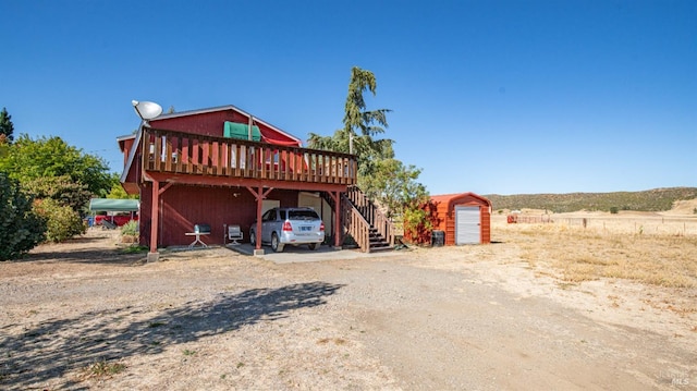 rear view of house featuring a garage, a wooden deck, an outbuilding, a rural view, and a carport