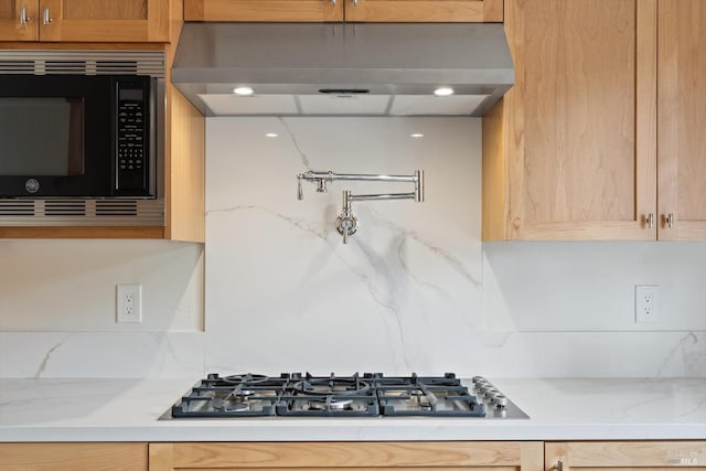 kitchen with black microwave, light stone counters, stainless steel gas stovetop, and range hood