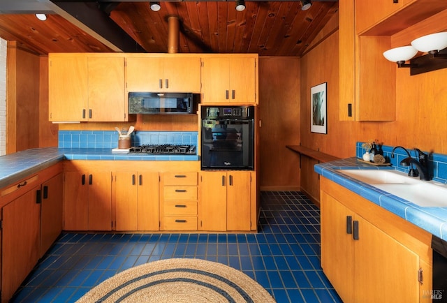 kitchen featuring wooden ceiling, black appliances, tile counters, wooden walls, and sink