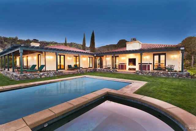 back house at dusk with a lawn and a patio