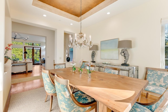 dining room with a tray ceiling, french doors, light hardwood / wood-style floors, and a notable chandelier