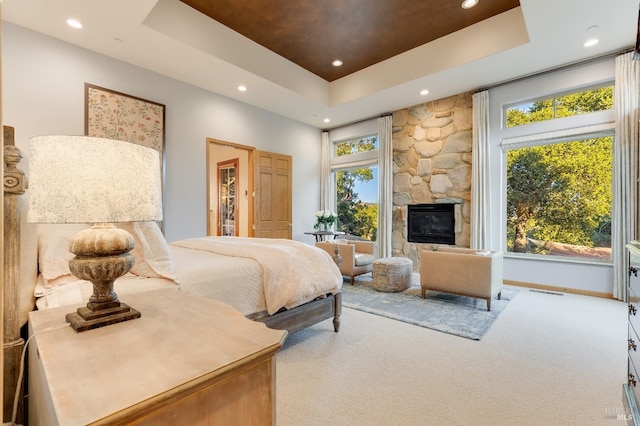 carpeted bedroom featuring baseboards, a stone fireplace, a tray ceiling, and recessed lighting
