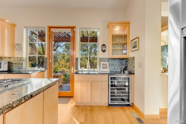 bar with a wealth of natural light, light wood finished floors, and beverage cooler