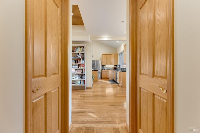 corridor featuring a sink, lofted ceiling, and light wood-style floors