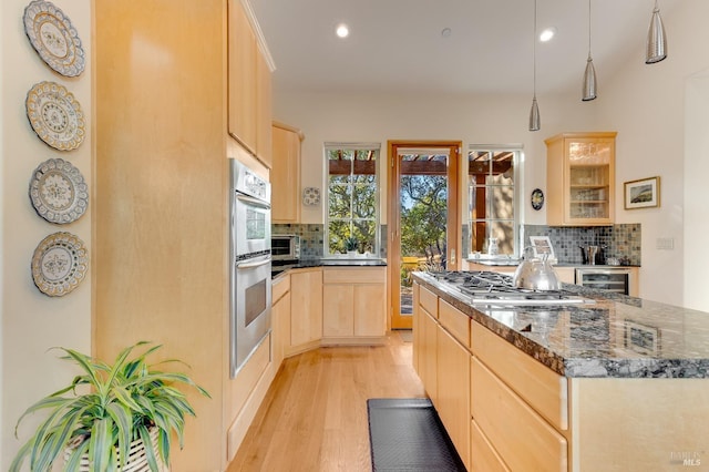 kitchen featuring light brown cabinets, stainless steel appliances, decorative backsplash, glass insert cabinets, and light wood-style floors