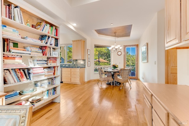 interior space with light wood-type flooring, a tray ceiling, and an inviting chandelier