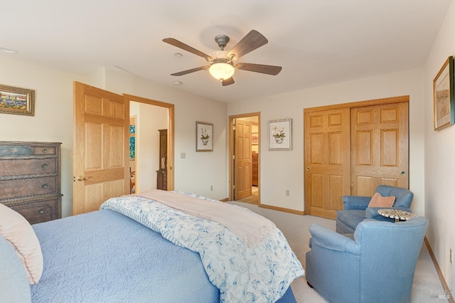 bedroom featuring baseboards, ceiling fan, a closet, ensuite bathroom, and light colored carpet