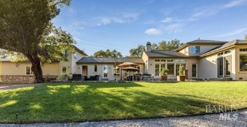 rear view of property with stucco siding, a chimney, and a lawn