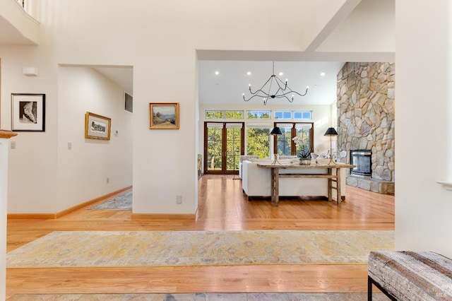 living room featuring an inviting chandelier, a towering ceiling, wood-type flooring, and a stone fireplace