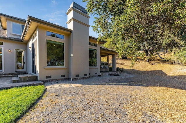 view of side of home with stucco siding, a chimney, and crawl space