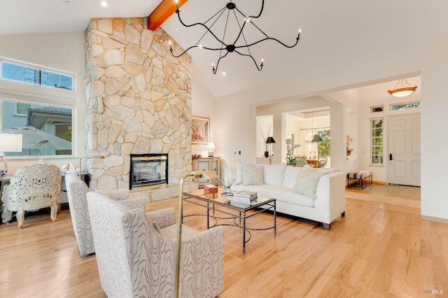 living area featuring beamed ceiling, a notable chandelier, a stone fireplace, and wood finished floors