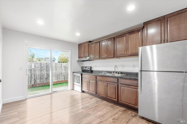 kitchen featuring dark stone counters, appliances with stainless steel finishes, sink, and light wood-type flooring