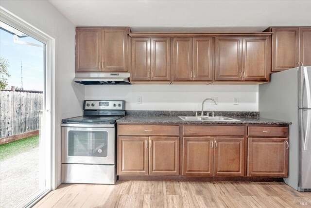 kitchen featuring dark stone countertops, appliances with stainless steel finishes, sink, and light hardwood / wood-style flooring