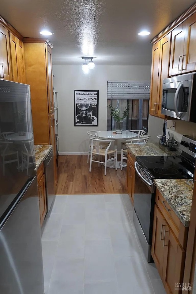 kitchen with light wood-type flooring, light stone counters, stainless steel appliances, and a textured ceiling