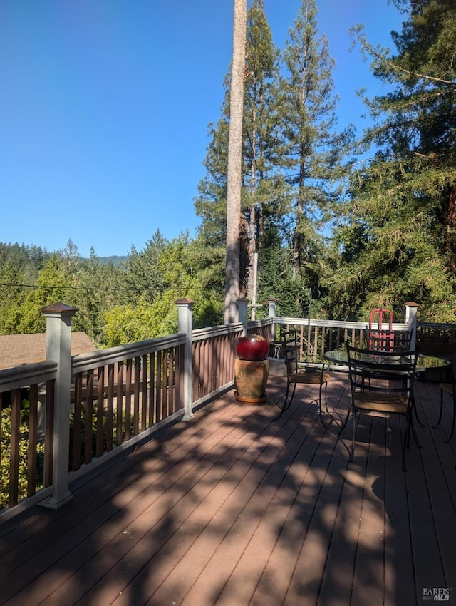 wooden terrace featuring a wooded view and outdoor dining space