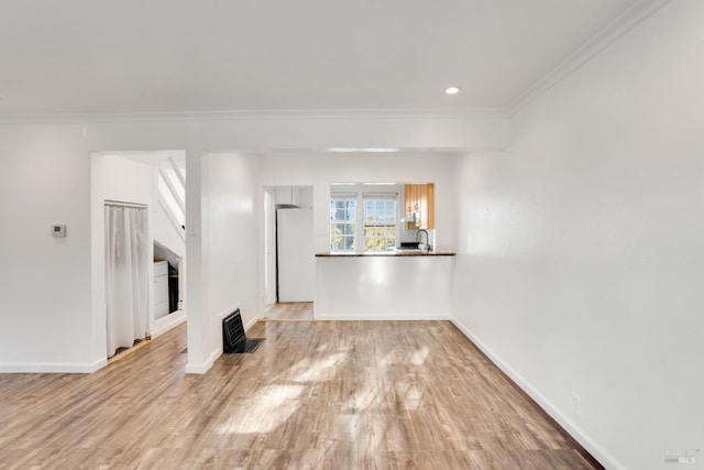 unfurnished living room featuring sink, light wood-type flooring, and crown molding