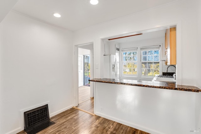 kitchen featuring heating unit, white refrigerator with ice dispenser, dark stone counters, sink, and hardwood / wood-style flooring