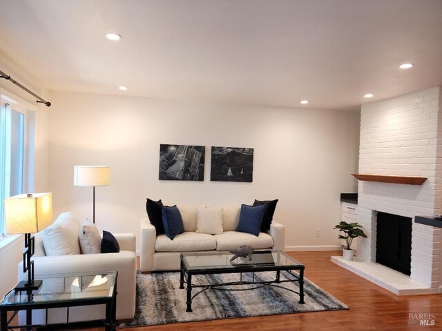 living room with a brick fireplace, wood-type flooring, and a healthy amount of sunlight