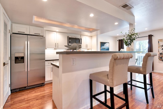 kitchen with white cabinets, appliances with stainless steel finishes, light wood-type flooring, and a kitchen bar