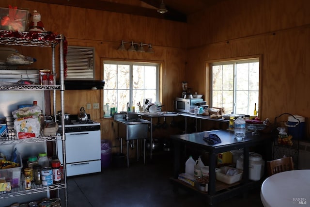 kitchen featuring white range with gas stovetop, sink, a wealth of natural light, and wood walls