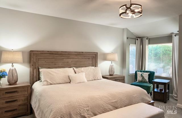 carpeted bedroom with an inviting chandelier and vaulted ceiling