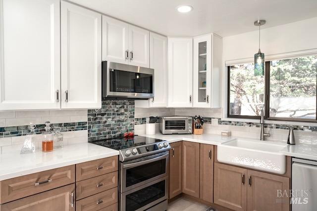 kitchen with white cabinetry, sink, stainless steel appliances, tasteful backsplash, and decorative light fixtures