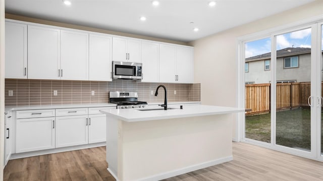 kitchen with sink, light wood-type flooring, an island with sink, stainless steel appliances, and white cabinets