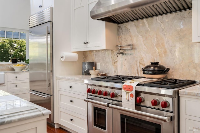 kitchen with extractor fan, premium appliances, and white cabinetry