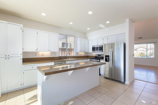 kitchen featuring white cabinetry, a center island, light tile patterned floors, appliances with stainless steel finishes, and dark stone counters