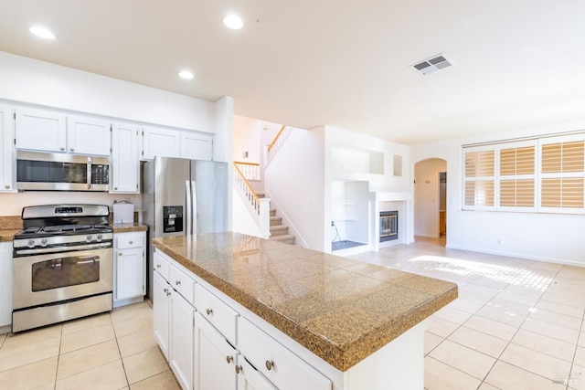 kitchen featuring stainless steel appliances, a kitchen island, light tile patterned floors, and white cabinets