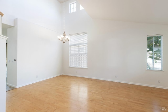 unfurnished room featuring an inviting chandelier, a high ceiling, and light wood-type flooring