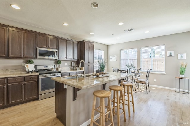 kitchen with a breakfast bar, a center island with sink, sink, light hardwood / wood-style flooring, and stainless steel appliances