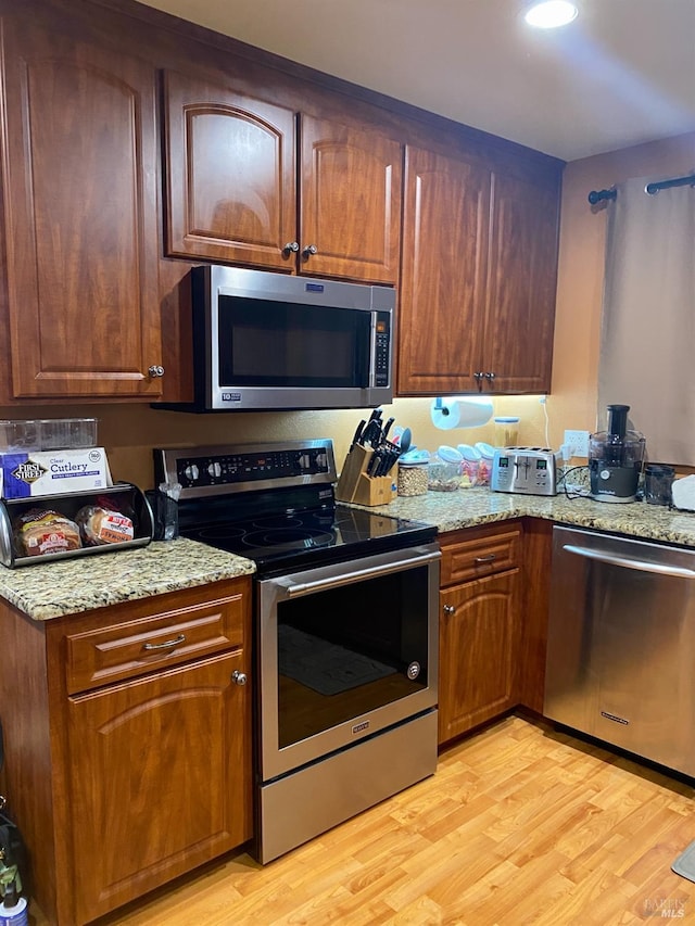 kitchen featuring light stone countertops, stainless steel appliances, and light wood-type flooring