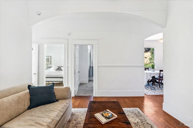 living area featuring baseboards, arched walkways, a high ceiling, and wood finished floors