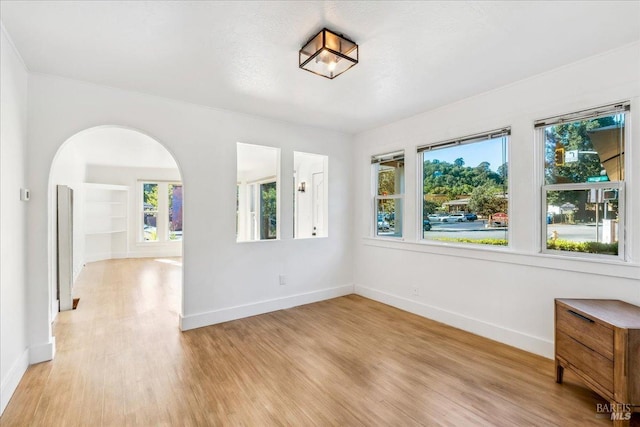 unfurnished room featuring arched walkways, built in features, light wood-style flooring, and baseboards